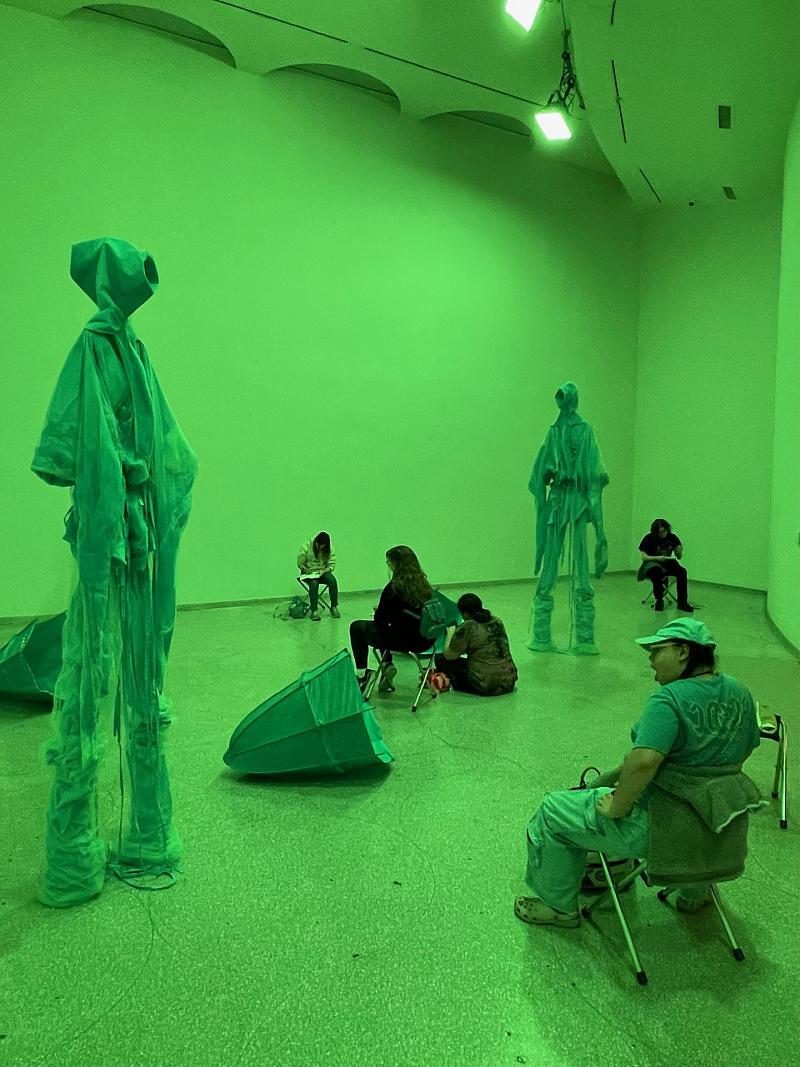 Students seated in various areas sketching sculptures inside a room illuminated with green light inside the Guggenheim museum