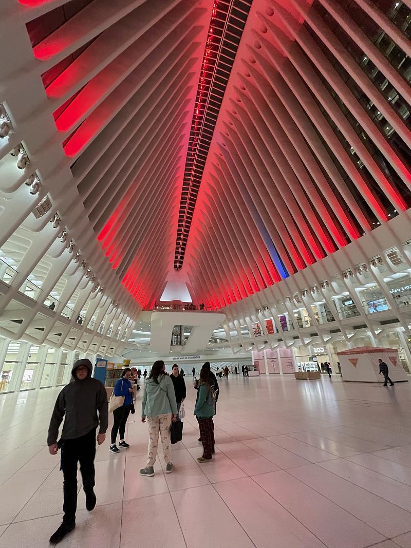 Students inside the Oculus, a large white structure with roof illuminated in red light