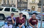 3 students sitting on bench with Fifth Avenue behind them